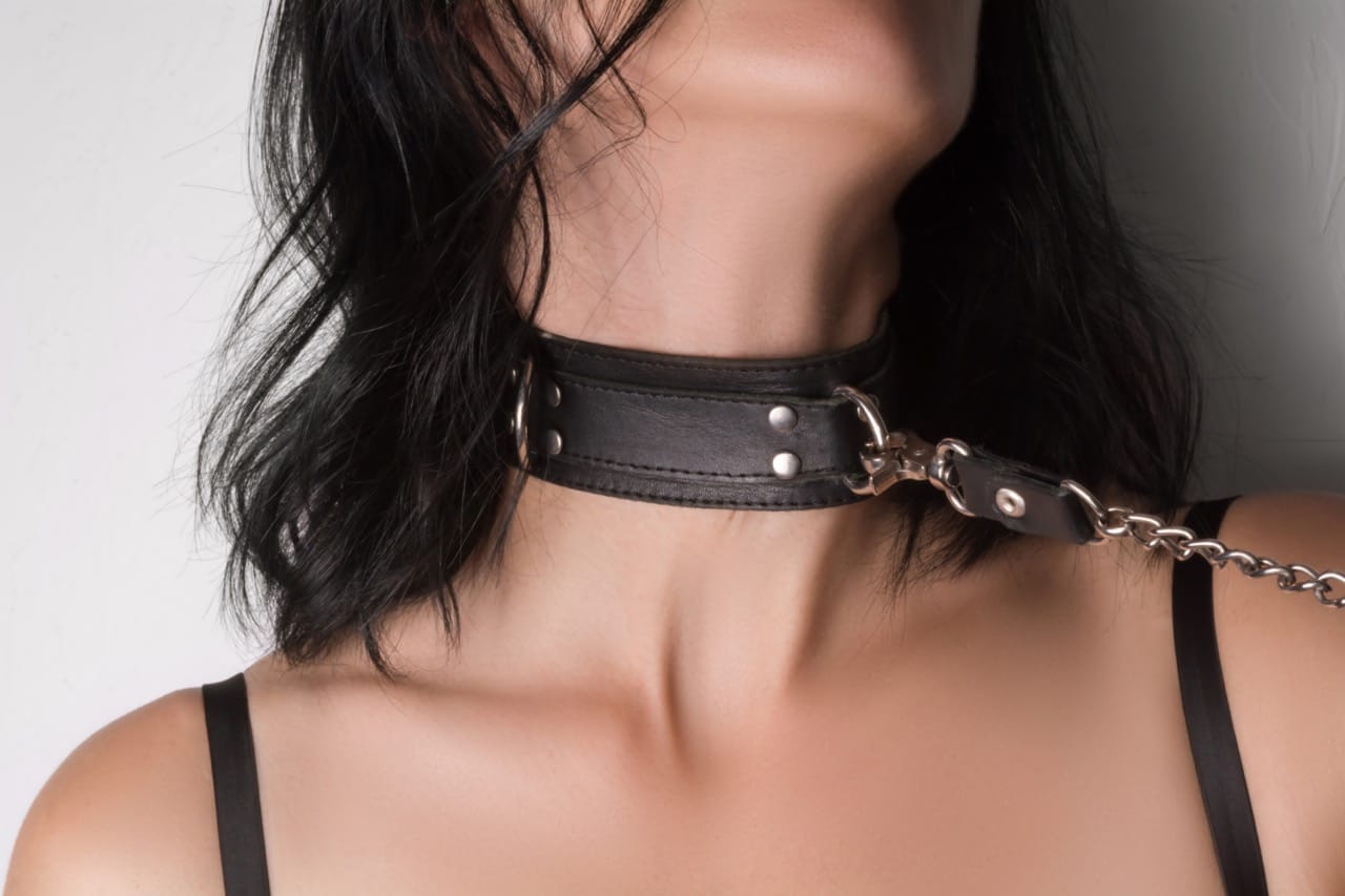 Close-up of a woman wearing a leather collar with chain, symbolizing submission, dominance, and the erotic tension explored in consensual choking and kink play.