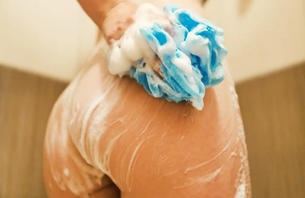 Close-up of a woman washing her butt in the shower with a foamy loofah — symbolizing anal hygiene and self-care before first-time anal sex