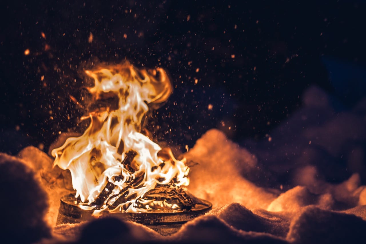 Bright fire crackling in the snow under a dark winter sky, glowing embers rising