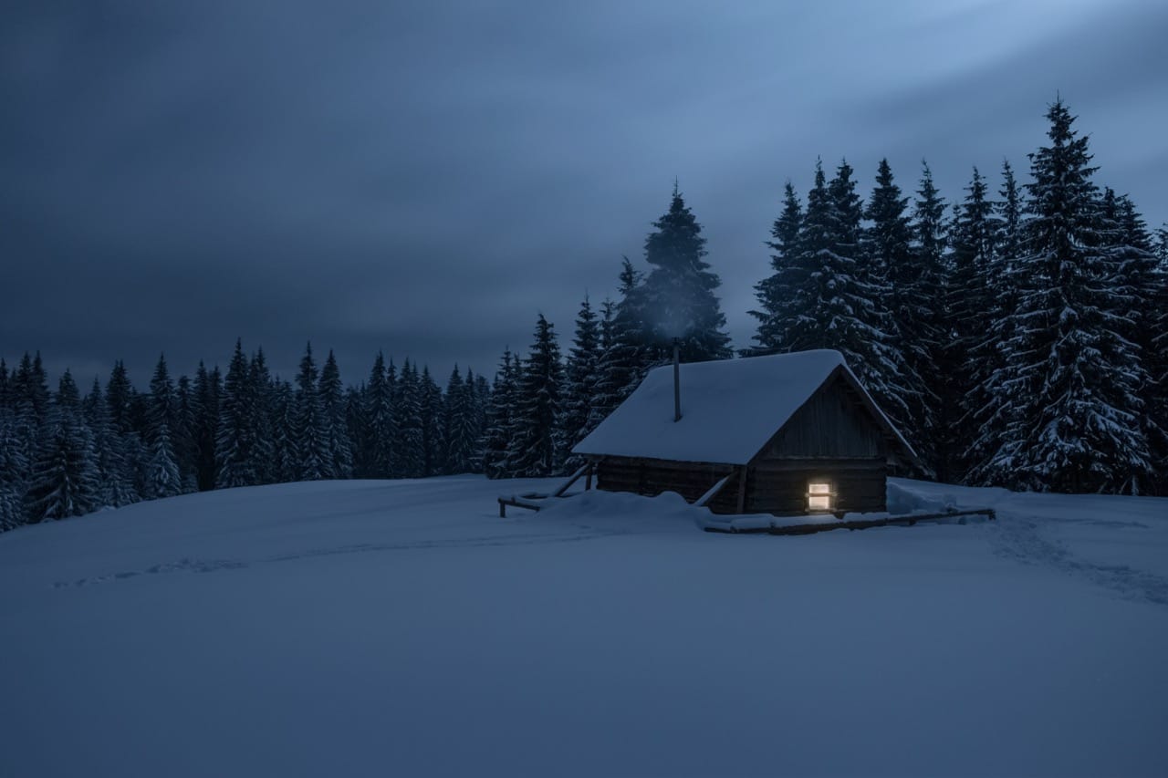 Glowing remote Montana cabin in snow near Yellowstone, setting for intimate blizzard survival.