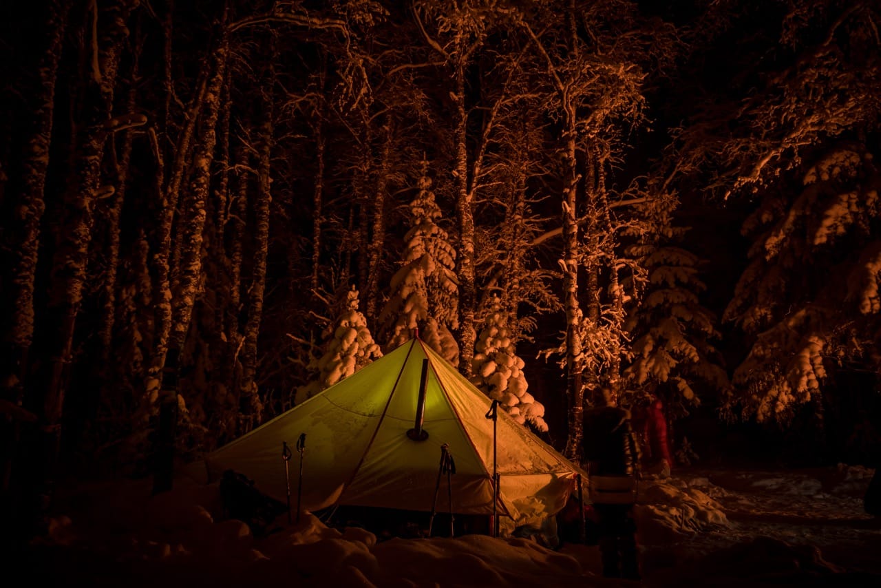 Lit emergency tent in snowy forest cave, hub of shared body heat in erotic winter adventure
